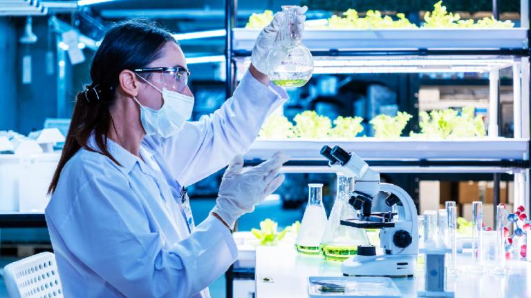 Científica con mascarilla y guantes trabajando con pipeta en un laboratorio iluminado